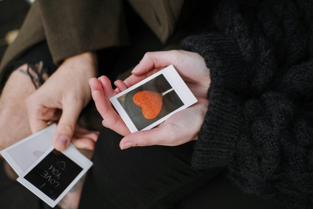 Close-up of hands holding heart-themed polaroids, symbolizing love and connection.